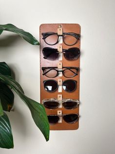 If you're looking for the perfect eyewear organizer for your home or office, our Handcrafted Leather Sunglasses Holder is the ideal solution. Meticulously crafted with attention to detail, this eyeglass stand combines functionality with elegant design, making it a standout addition to any space. ✦ Dimensions: Compact Size: 40 x 15 cm / 15,7 x 5,9 inch 6 Compartments: Ample storage for up to six pairs of sunglasses or eyeglasses. ✦ Handcrafted Quality: Each sunglasses holder is meticulously crafted by skilled artisans, reflecting our commitment to high-quality craftsmanship. Made with vegetal leather, this glasses holder ensures durability and long-lasting use. ✦ The Perfect Gift: Searching for a unique and stylish gift? Our handcrafted leather sunglasses holder is an excellent choice. It's Sun Glass Holder, Sunglasses Stand, Eye Glass Holder, Wood Eyeglass Holder, Wooden Sunglasses Holder, Sunglasses Hanger, Eyewear Shop Design, Eyeglass Holder Stand Wood, Eyeglass Holder Stand