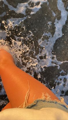 a woman's legs with water splashing on them and her feet in the sand