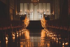 an aisle lined with chairs and candles in front of a chandelier filled with lit candles