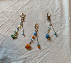 four charms are hanging from chains on a white sheet with a star and fish design