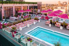 an outdoor pool with tables and umbrellas next to the swimming pool in front of a cityscape