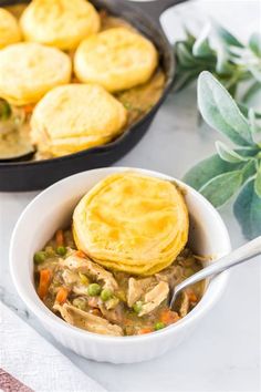 a bowl filled with chicken pot pies next to a skillet full of biscuits