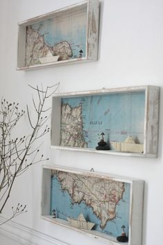 three framed maps are hanging on the wall above a vase with dried flowers in it