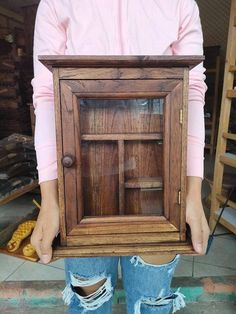 a person holding up a small wooden cabinet in their hands, with the door open