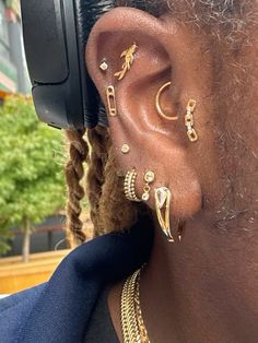 a close up of a person with ear piercings on their ears and wearing gold jewelry