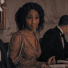 a woman sitting at a table in front of a man wearing a tuxedo