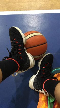 a person's feet in black and red sneakers with basketballs on the floor