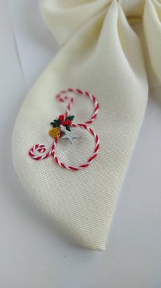 a white bow tie with a red and white striped ribbon on the side, next to it is an embroidered ornament