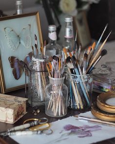 there are many pens and pencils in the glass jar on the table with other items