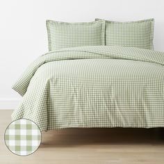 a green and white checkered comforter set on a wooden floor next to a window