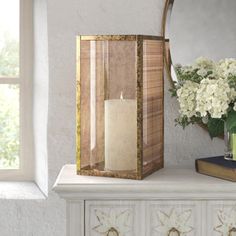 a vase with white flowers and a candle on a dresser next to a mirror in a room