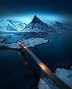 an aerial view of a bridge over water with snow covered mountains in the background at night