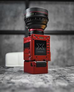 a red camera sitting on top of a table next to a large lens mounted into it's body