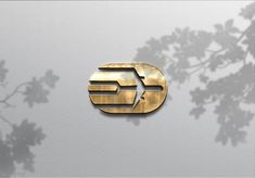 the letter e is inscribed in gold on a white background with shadows from leaves and branches