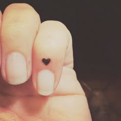 a person's hand with a black heart tattoo on their thumb and one finger