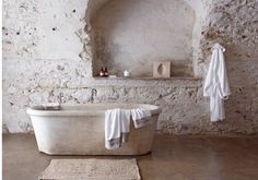 an old bathtub with towels hanging on the wall next to it and a rug in front of it