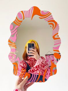 a woman taking a selfie with her cell phone in front of a colorful mirror