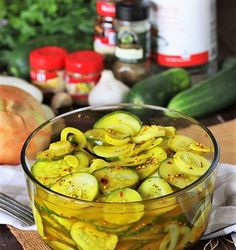 a glass bowl filled with pickles on top of a wooden table next to vegetables