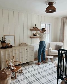 a woman is painting the wall in her bedroom with white walls and plaid rugs