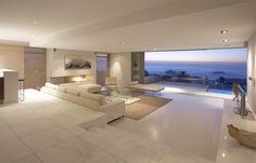 a living room filled with furniture and a large window overlooking the ocean at night time