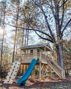 a blue slide in the woods next to a tree house with a deck and stairs