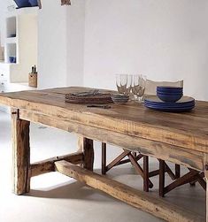 a wooden table with plates, glasses and napkins on it in a white room