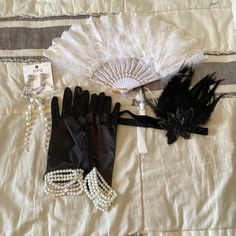 an assortment of accessories including gloves, pearls and a fan on a white bed sheet