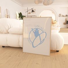 a white couch sitting next to a framed poster on top of a hard wood floor