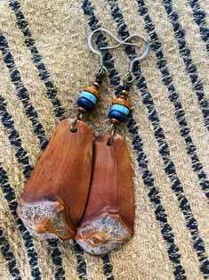 two wooden earrings with beads hanging from them on a striped cloth surface, one is made out of wood and the other has metal earwires