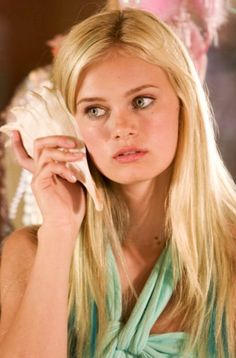 a beautiful blond woman holding a seashell in her hand and looking at the camera