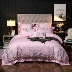 a bed with pink comforter and pillows on top of it in front of a black wall