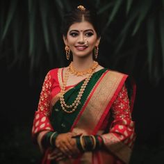 a woman in a green and red sari with gold jewelry on her head, smiling at the camera