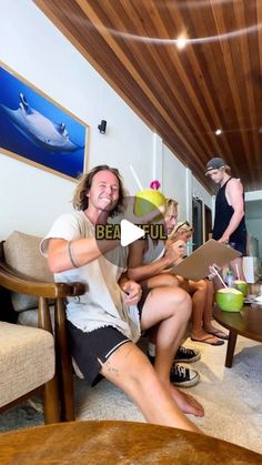 three people sitting in a living room and one is holding up a sign with the word beautiful written on it