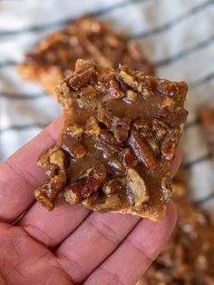 a hand holding up a piece of chocolate covered granola bar with nuts on top