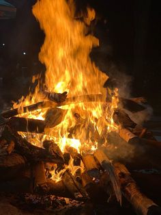 the fire is blazing in the dark with lots of wood and logs on it's sides