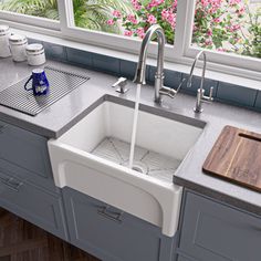 a kitchen sink sitting under a window next to a cutting board on top of a counter