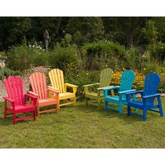 four colorful adironda chairs sitting on the grass in front of some bushes and flowers