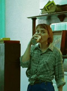 a woman standing in front of a mirror drinking from a cup