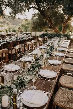 a long table with plates and place settings set up for an outdoor wedding reception under the trees