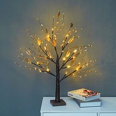 a lighted tree on top of a white table next to a book and a gray wall