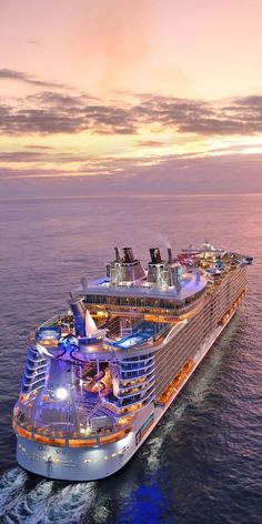 a large cruise ship in the middle of the ocean at sunset with its lights on