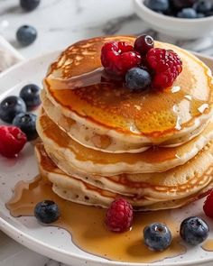 a stack of pancakes with syrup and berries on a plate next to some blueberries