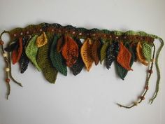 an assortment of crocheted leaves are hanging on the side of a white wall