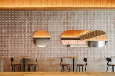 three round mirrors are hanging on the wall above four wooden stools in a restaurant