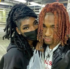 two people wearing face masks in a subway station, one with dreadlocks and the other without