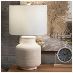 a white vase sitting on top of a wooden table next to a clock and lamp