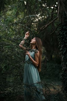 a woman standing in the woods with her hands up to her face and looking up