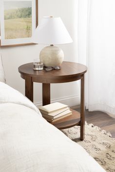 a small table with a lamp on it next to a bed and a painting in the background