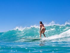 a woman riding a surfboard on top of a wave in the ocean with blue sky