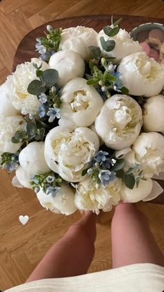 a bridal bouquet with white flowers and greenery in someone's hand on a wooden floor